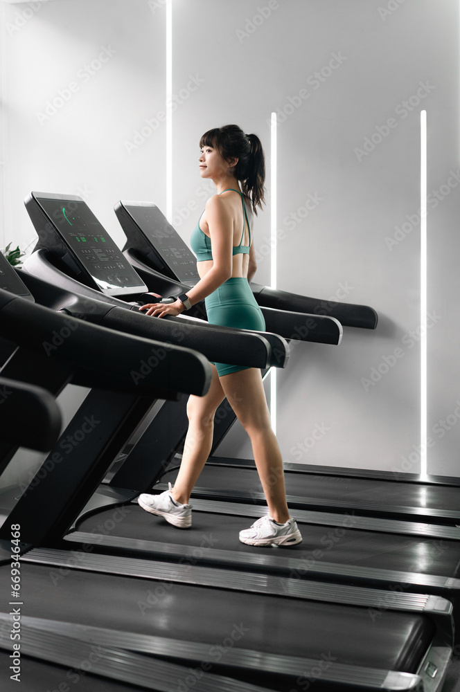 Asian woman is running on treadmill in gym.