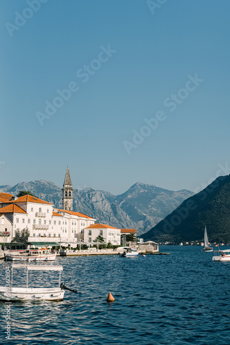 Boats are moored in the sea off the coast of Perast with old houses and a church bell tower. Montenegro © Nadtochiy