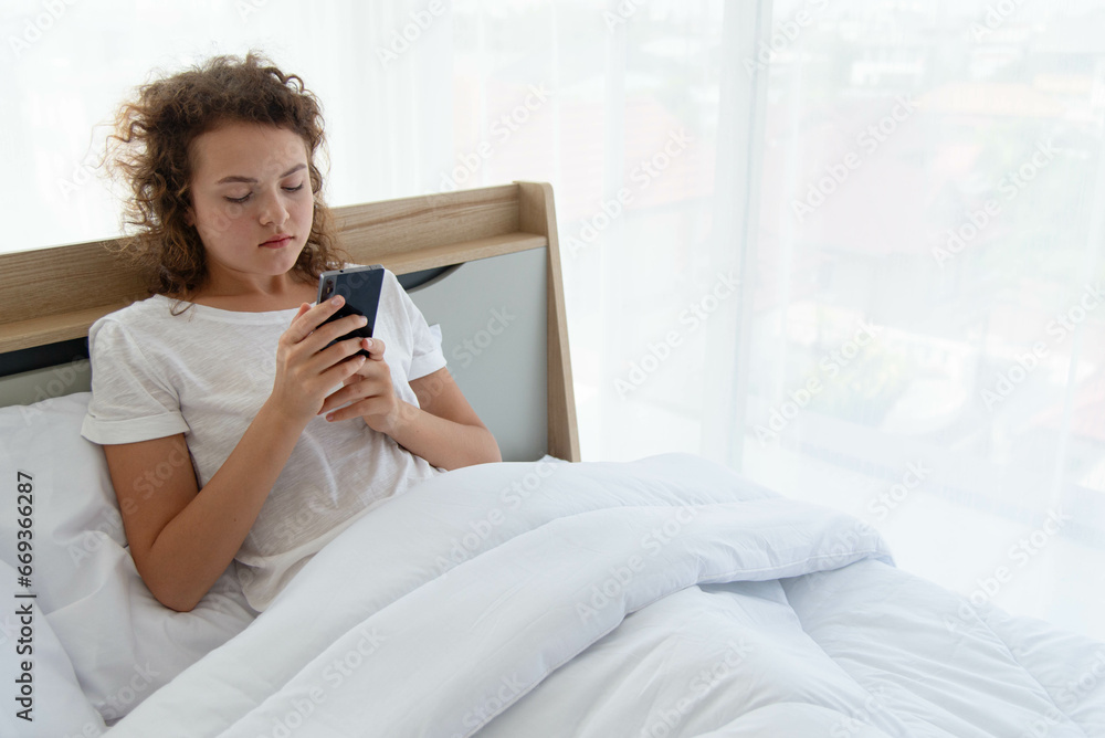 Young beautiful happy woman relaxing and using smartphone while lying in bed in the morning after waking up. Young beautiful happy woman relaxing and using smartphone while lying in bed in the morning after waking up.