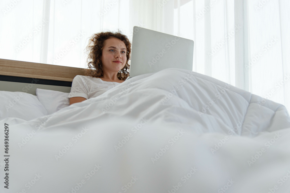 Young beautiful happy woman relaxing and working with laptop while lying in bed in the morning after waking up. Young beautiful happy woman relaxing and working with laptop while lying in bed in the morning after waking up.