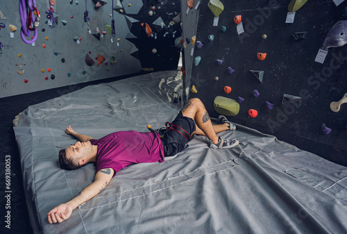 A strong female climber relax near artificial wall with colorful grips and ropes.