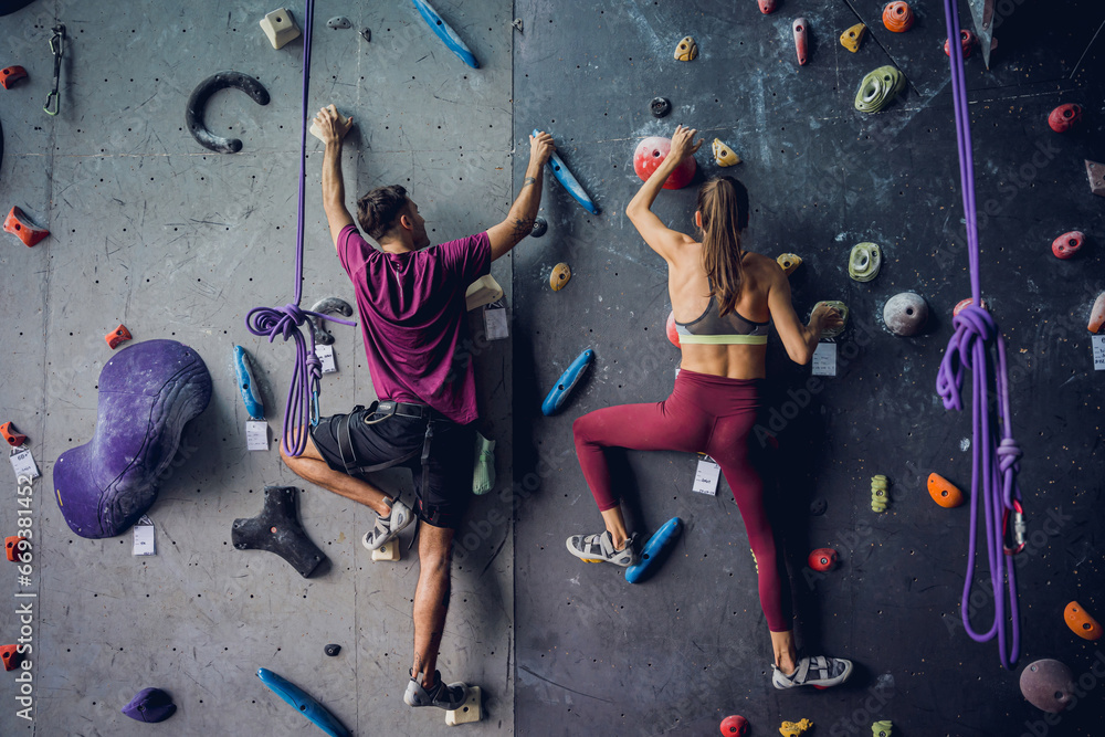 A strong couple of climbers climb an artificial wall with colorful grips and ropes. A strong couple of climbers climb an artificial wall with colorful grips and ropes.