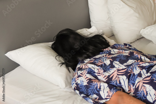 Fotografie Long haired asian man is sleeping with prone position on a bed with a white pillow