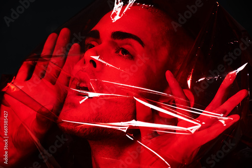 Man, red plastic and suffocating in studio isolated on black background. Polyethylene, film or person with depression, social isolation and anxiety, stress or mental health crisis, psychology or neon photo