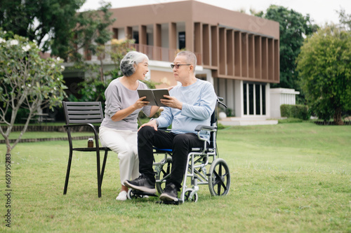 Asian Senior couple sitting in wheelchairs taking care of each other.in romantic time They laughing and smiling while sitting outdoor in park.. © laddawan