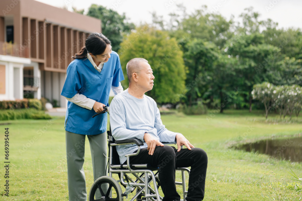 Elderly asian senior woman on wheelchair with Asian careful caregiver and encourage patient, walking in garden. with care from a caregiver Elderly asian senior woman on wheelchair with Asian careful caregiver and encourage patient, walking in garden. with care from a caregiver