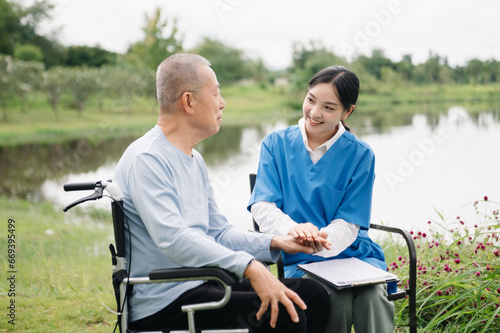 Asian careful caregiver or nurse and the happy patient in a wheelchair are walking in the garden. to help and encourage and rest your mind with green nature. Use a stethoscope to listen