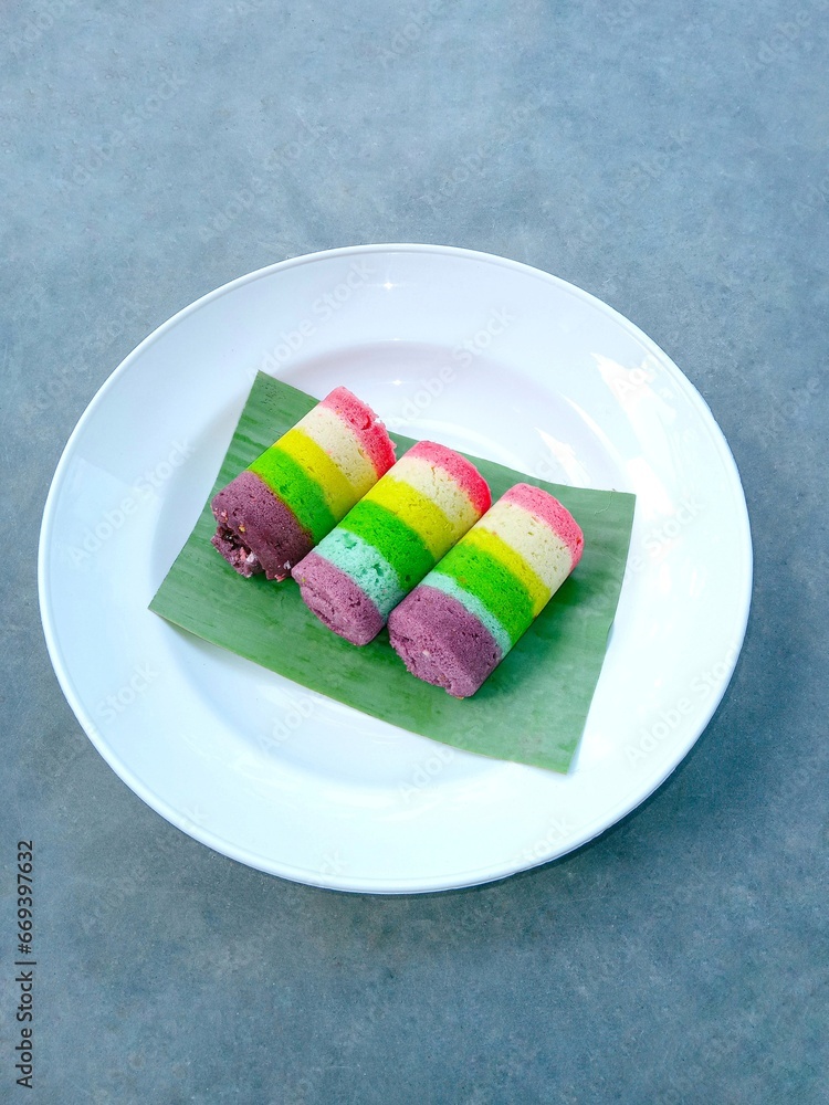 roll cake. Sweet cake. Mini rainbow roll cake on plate over gray background. Vertical shot. Colorful cake roll cake. Sweet cake. Mini rainbow roll cake on plate over gray background. Vertical shot. Colorful cake