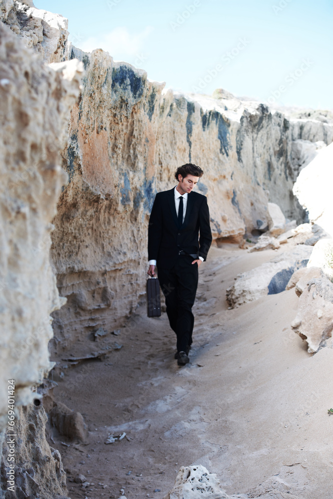 Travel, briefcase and business man at a beach for thinking, reflection or enjoying break outdoor. Nature, rock and young male entrepreneur walking in a suit for fresh air, getaway or peaceful morning