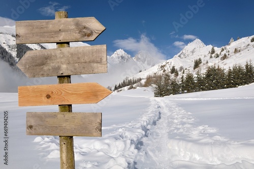 wooden directional post sign with arrow in  front of snowy mountain landscape © coco