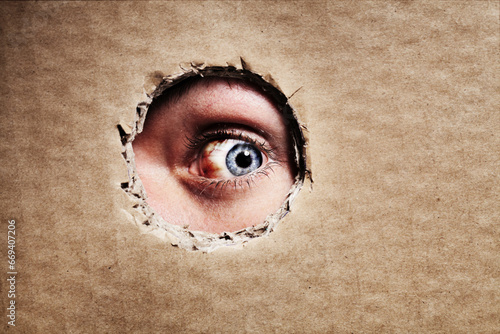 Closeup, cardboard and eye spy on hole, peek and search on mockup space. Face, macro and man peeping through paper board for secret, security and watch for surveillance, discover mystery and privacy photo