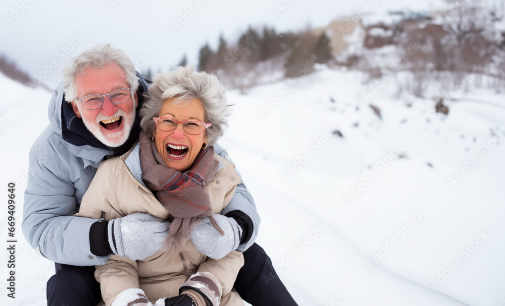 Fototapeta premium Senior couple looking happy outside in the snow, maybe out sledding or going for a walk. Concept of winter and mature happiness. Shallow field of view with copy space.