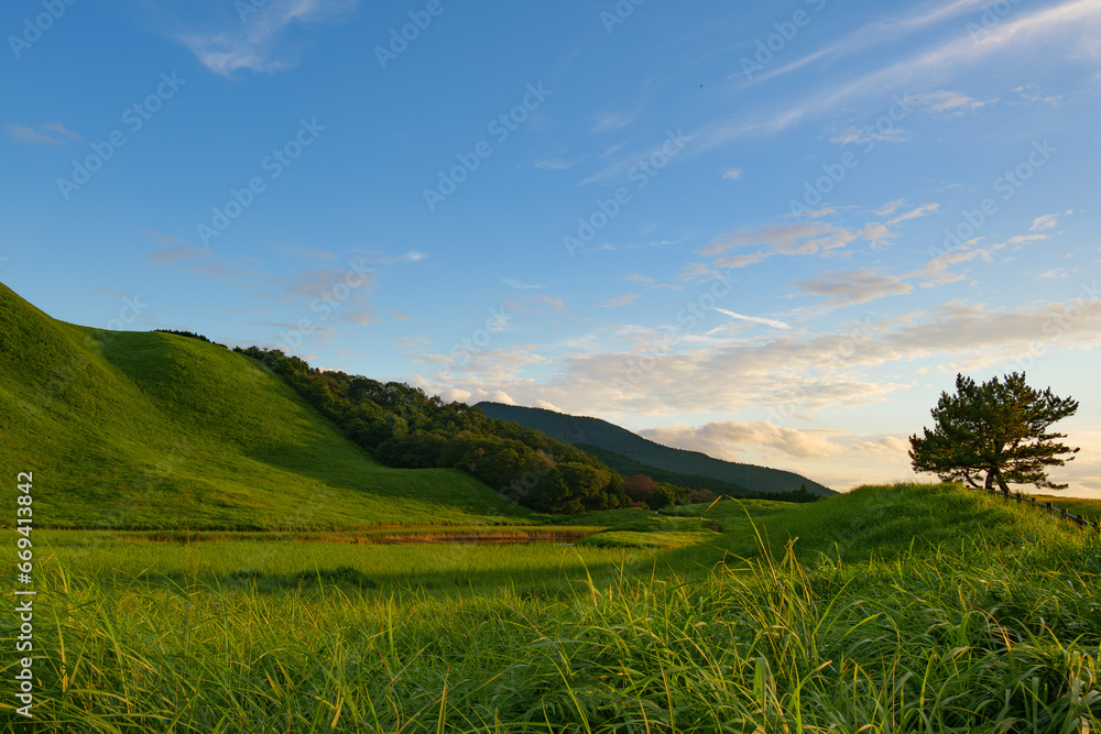 A summer landscape of green meadows, beautiful mountains, and golden cloudy sunsets.