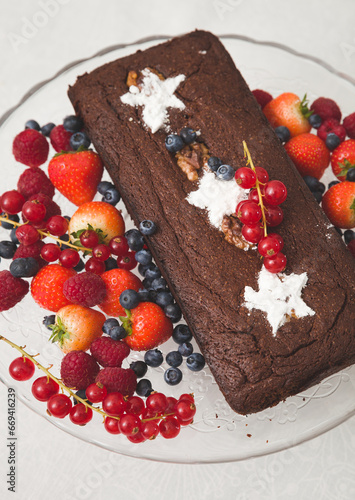 Chocolate brownie cake with fresh blueberries, raspberries, strawberries, red currant and white stars made of powdered sugar. Homemade cake decorated with fruit. Festive concept