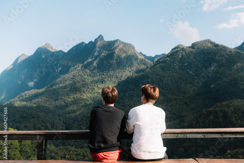 Rear view image of two male traveler sitting and looking at a beautiful mountain,sky field and nature view