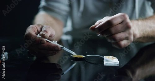 Hands, drugs and heroin with an addict closeup on a dark background to inject narcotics using a syringe. Depression, drug abuse and a spoon to melt an opioid for injection with a needle to get high photo