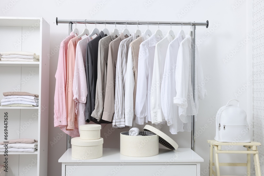 Wardrobe organization. Rack with different stylish clothes, chest of drawers and folding ladder near white wall indoors Wardrobe organization. Rack with different stylish clothes, chest of drawers and folding ladder near white wall indoors