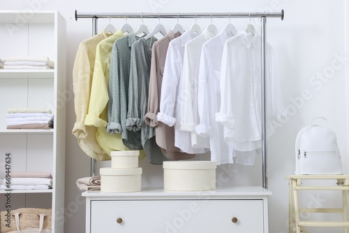 Wardrobe organization. Rack with different stylish clothes, chest of drawers and folding ladder near white wall indoors © New Africa