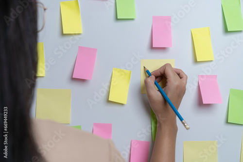 Creative woman writing on blank sticky notes on the wall