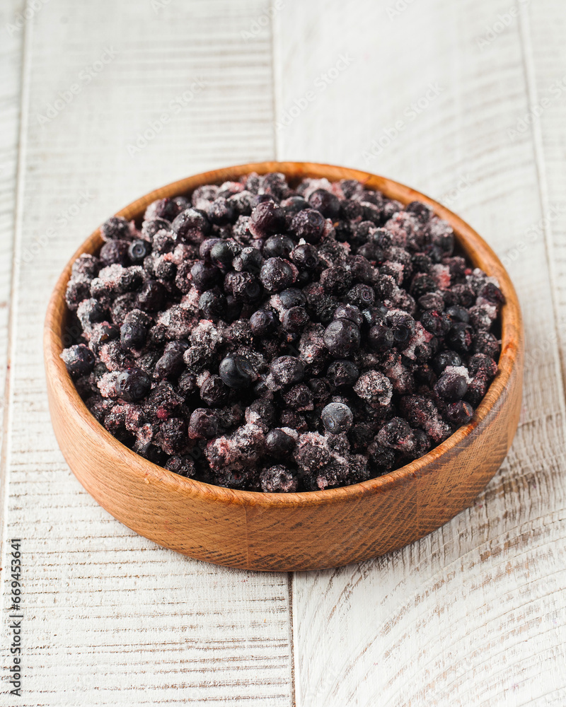 Frozen black currant in a wooden bowl on a white wooden background. Berries, frozen foods. Frozen black currant in a wooden bowl on a white wooden background. Berries, frozen foods.