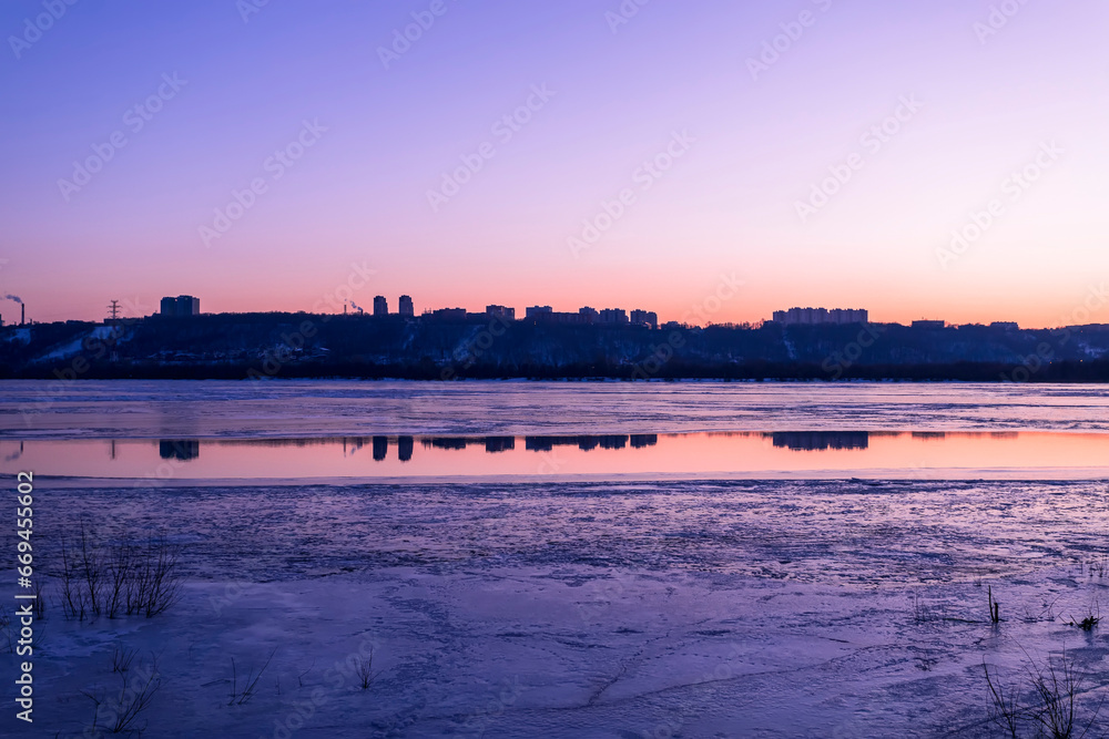 City silhouette on sunset background with houses. Silhouette of an evening city on a frozen river background on a spring evening