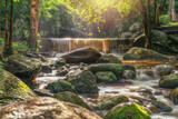 Waterfall in lush forest with golden sunlight shining down on stream surrounded by beautiful trees.