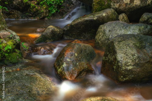 Waterfall in lush forest with golden sunlight shining down on stream surrounded by beautiful trees.
