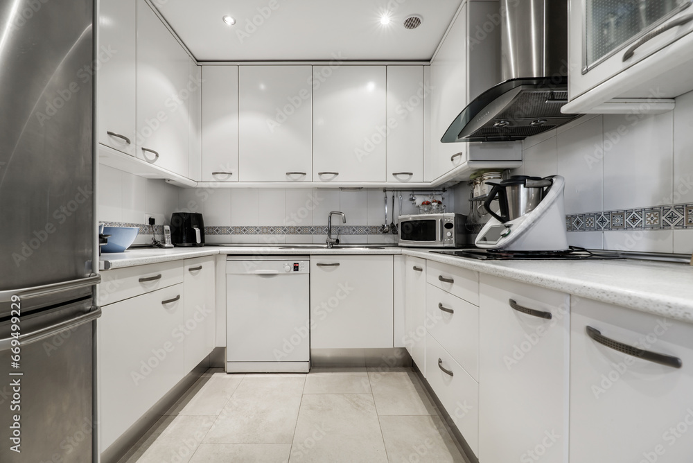 Fototapeta premium Furnished U-shaped kitchen with white cabinets and integrated stainless steel appliances and small appliances on the countertop