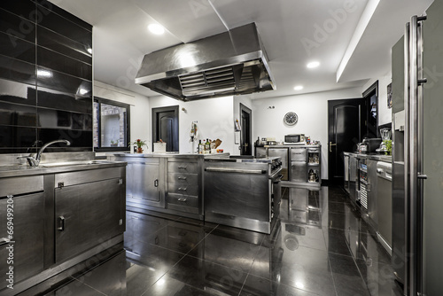 Kitchen of a single-family home furnished with industrial stainless steel furniture and a large extractor hood on the ceiling