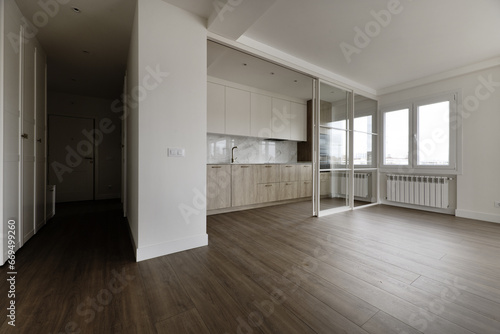 Kitchen furnished with white cabinets in the upper part and wooden ones in the lower part and integrated black appliances  many windows and glass separating screen