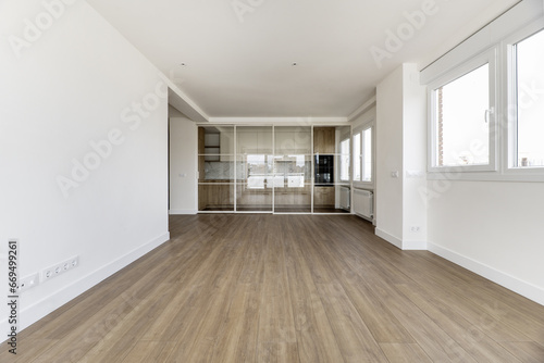 Empty living room of an apartment with a kitchen with a glass screen and retractable white metal