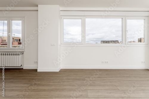 Wall full of windows with views of a living room with wooden floors and plain white painted walls