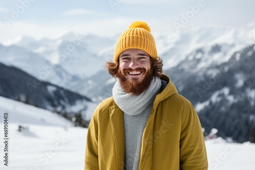 A handsome red-haired young man in a knitted yellow hat walks and smiles in a snowy winter mountains. Happy guy's face portrait close-up front view. Generative AI. Outdoor activities concept.