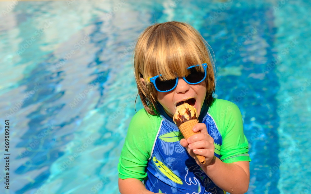 A boy eats an ice cream cone near the pool. The child enjoys the holidays and sweets. Bright summer, positive emotions A boy eats an ice cream cone near the pool. The child enjoys the holidays and sweets. Bright summer, positive emotions