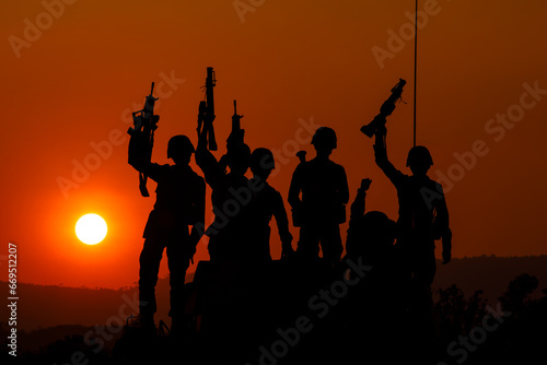 silhouette group of special forces sodiers standing and sit holding gun on cannon tank with over the sunset and colorful orange sky background,