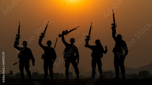 silhouette group of special forces sodiers standing and holding gun over the sunset and colorful orange sky background