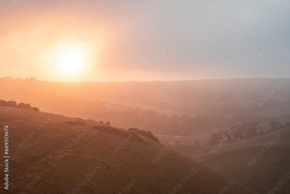 Stunning Summer sunrise from Devil's Dyke in South Downs National Park in English countryside with low lying clouds giving moody feeling