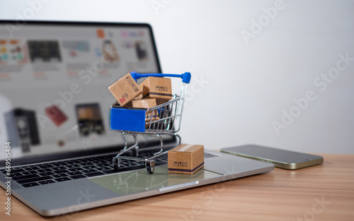 Shopping cart and product boxes placed on laptop computer represent online shopping concept, website, e-commerce, marketplace platform, technology and online payment concept.