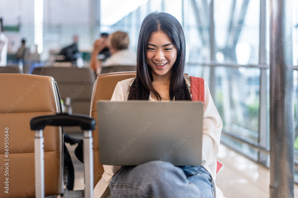 Portrait Of Happy Traveling young asian woman with laptop for work sits on chair waiting for flight in terminal hall area, she checks information and emails before boarding plane, traveler concept.