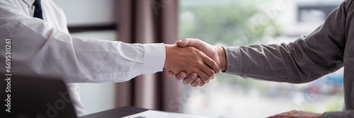 Businessman real estate seller and business shaking hands together after reading property investment document to discussion about deal agreement terms data of home sales contract and home insurance