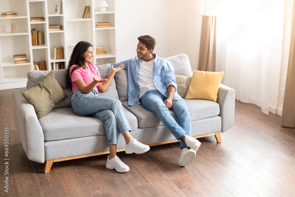 Indian couple chatting animatedly on their living room sofa