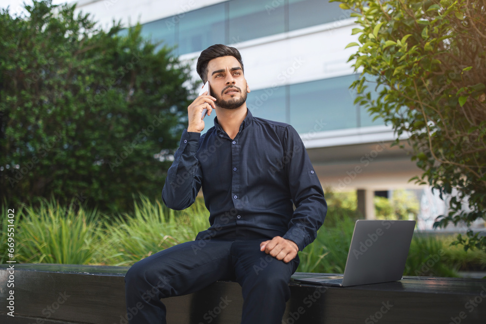 Middle eastern business man communicating via phone with laptop outside Middle eastern business man communicating via phone with laptop outside
