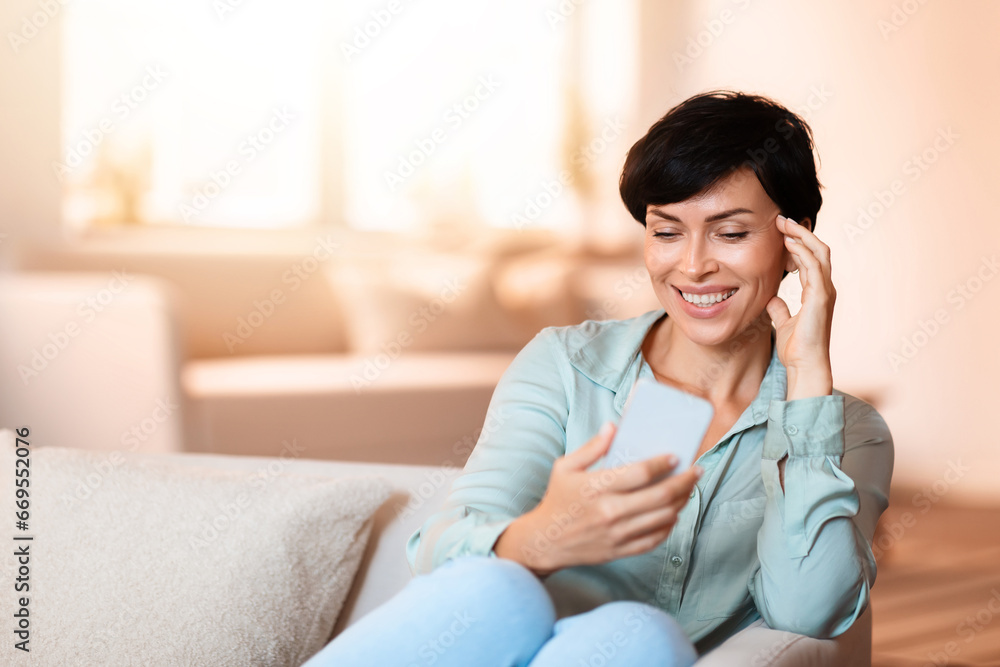 Middle aged European woman scrolling on smartphone in living room Middle aged European woman scrolling on smartphone in living room