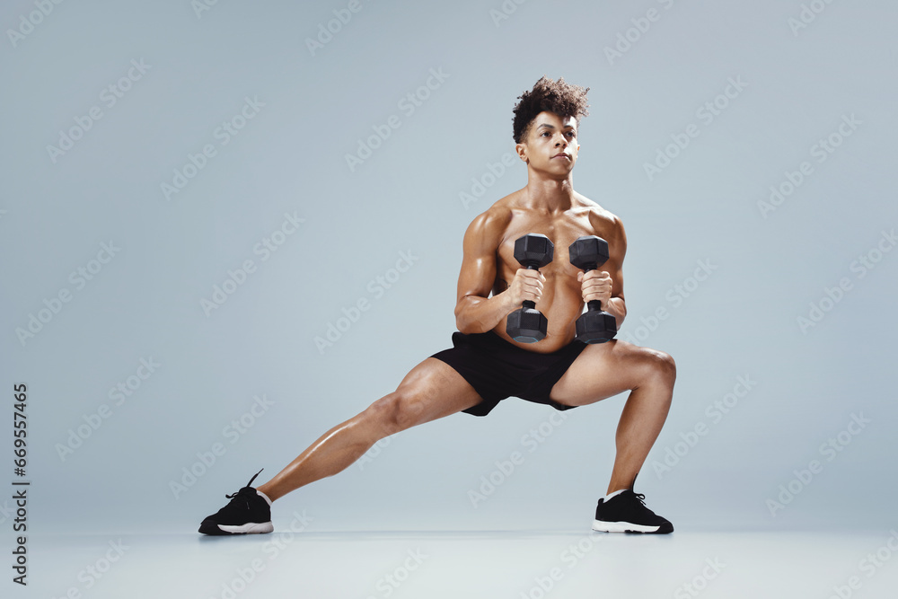 Athletic young man performing deep lunge while holding dumbbells, studio