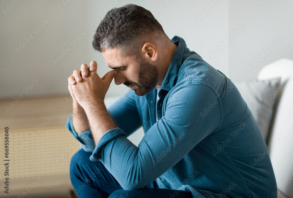 Depressed middle aged man sitting on sofa in living room Depressed middle aged man sitting on sofa in living room