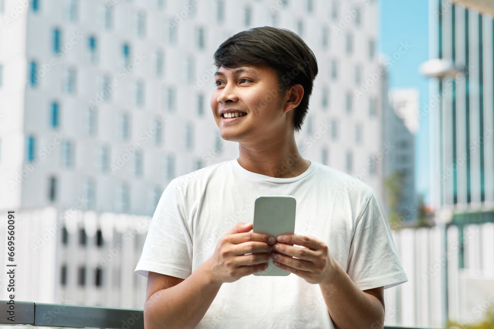 Happy young asian man using smartphone, posing at urban area