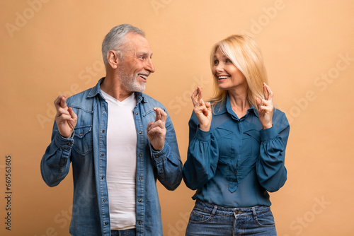 Happy senior man and woman crossing fingers, beige background photo