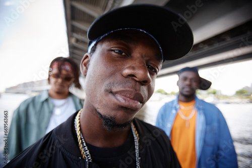 Fotografie Young stylish leader of hip hop boy band in black cap looking at camera while pe