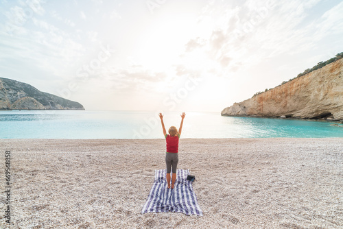 Woman performing yoga exercises on a beautiful empty beach in Greece. Dramatic coastline scenic bay rocky cliffs in the Ionian islands.
