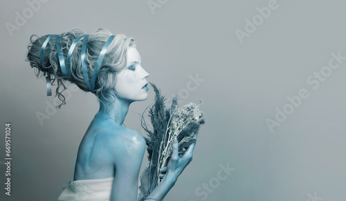 Pretty young Snow Queen woman actress with stage makeup and hairstyle on blue banner background. Halloween, carnival, performance and theater concept